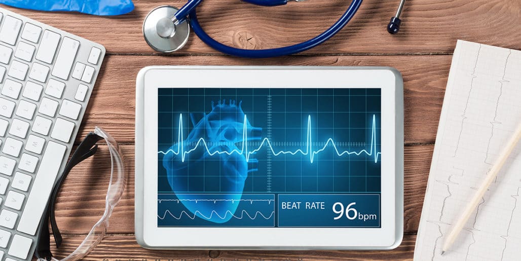 A tablet displaying a digital heart rate monitor and EKG readout on a medical desk, representing a Fortune 500 healthcare provider in a Strategic Benefits Advisors case study on selecting an AI cognitive assistant.