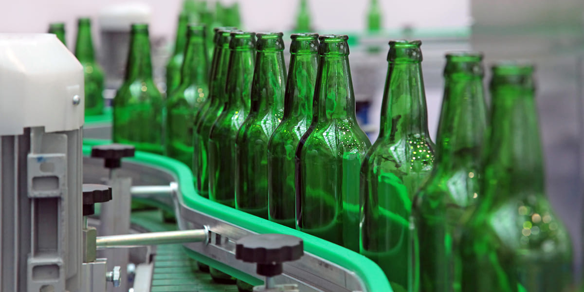 A row of empty green glass bottles moving along a manufacturing conveyor belt, representing a Fortune 500 food and beverage client in a Strategic Benefits Advisors case study on fixing pension data errors and rebuilding participant files.