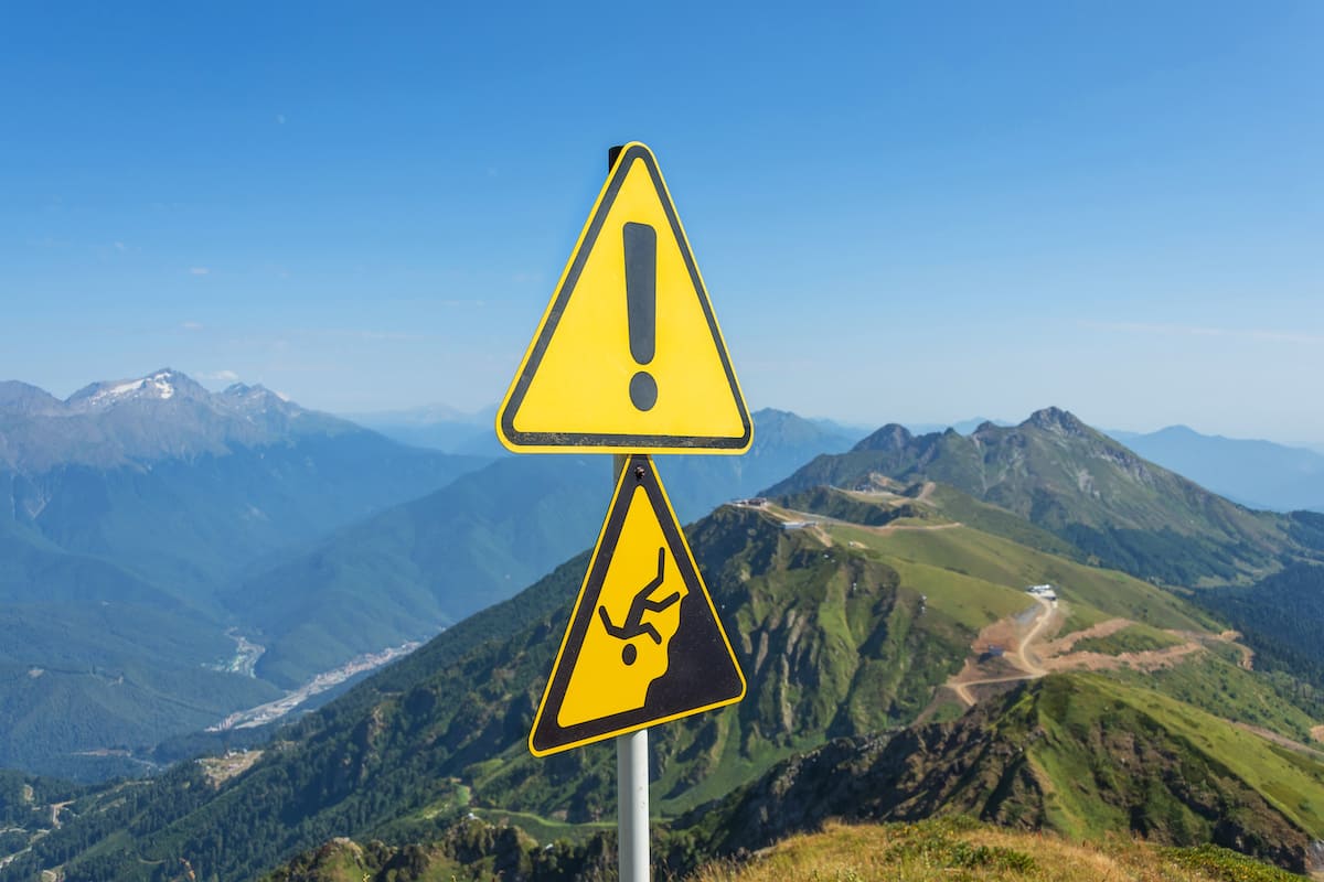 Strategic Benefits Advisors article graphic regarding hidden retirement plan governance risks, featuring a yellow warning exclamation point sign and a falling-person warning sign set against a backdrop of steep mountain peaks.