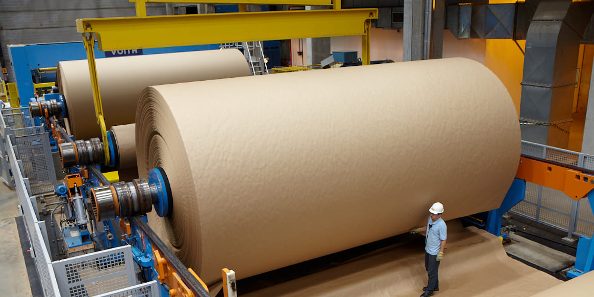 Resolving uncashed checks to complete a frozen pension plan termination, featuring massive brown paper rolls on an industrial manufacturing assembly line with a worker.