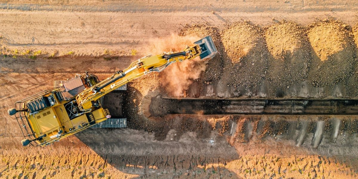 Reducing retirement-age participant backlogs and RMD exposure for an industrial manufacturing client, featuring an aerial top-down view of a large yellow excavator digging a trench.
