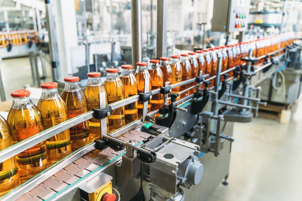 Strategic Benefits Advisors case study regarding fixing service date errors for a complex union workforce, showing glass bottles with red caps moving along an automated conveyor belt in a manufacturing facility.