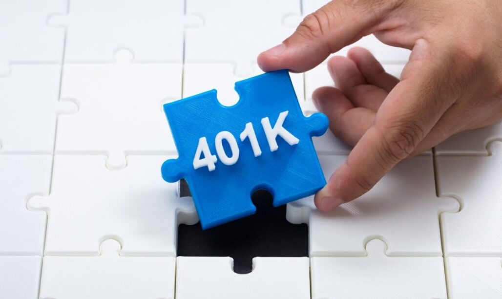 Strategic Benefits Advisors article graphic, showing a hand placing a bright blue puzzle piece labeled "401K" into a missing slot of a white jigsaw puzzle.