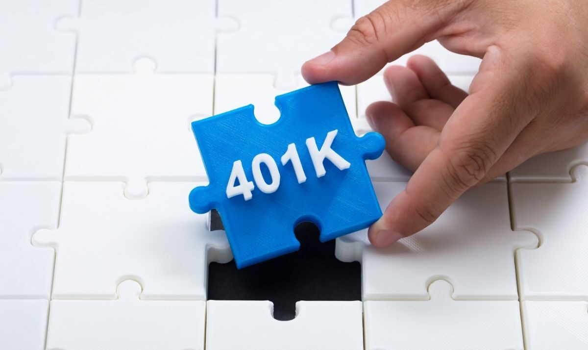 Strategic Benefits Advisors article graphic, showing a hand placing a bright blue puzzle piece labeled "401K" into a missing slot of a white jigsaw puzzle.