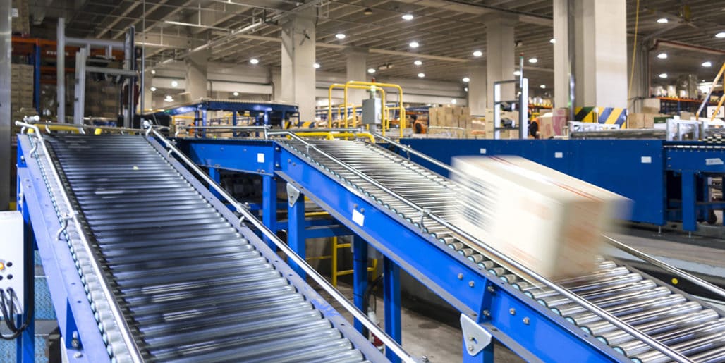 Strategic Benefits Advisors case study regarding correcting pension and 401(k) errors under the IRS Self-Correction Program for a Fortune 100 manufacturer, showing a cardboard box moving down a blue conveyor belt in a distribution and manufacturing facility.