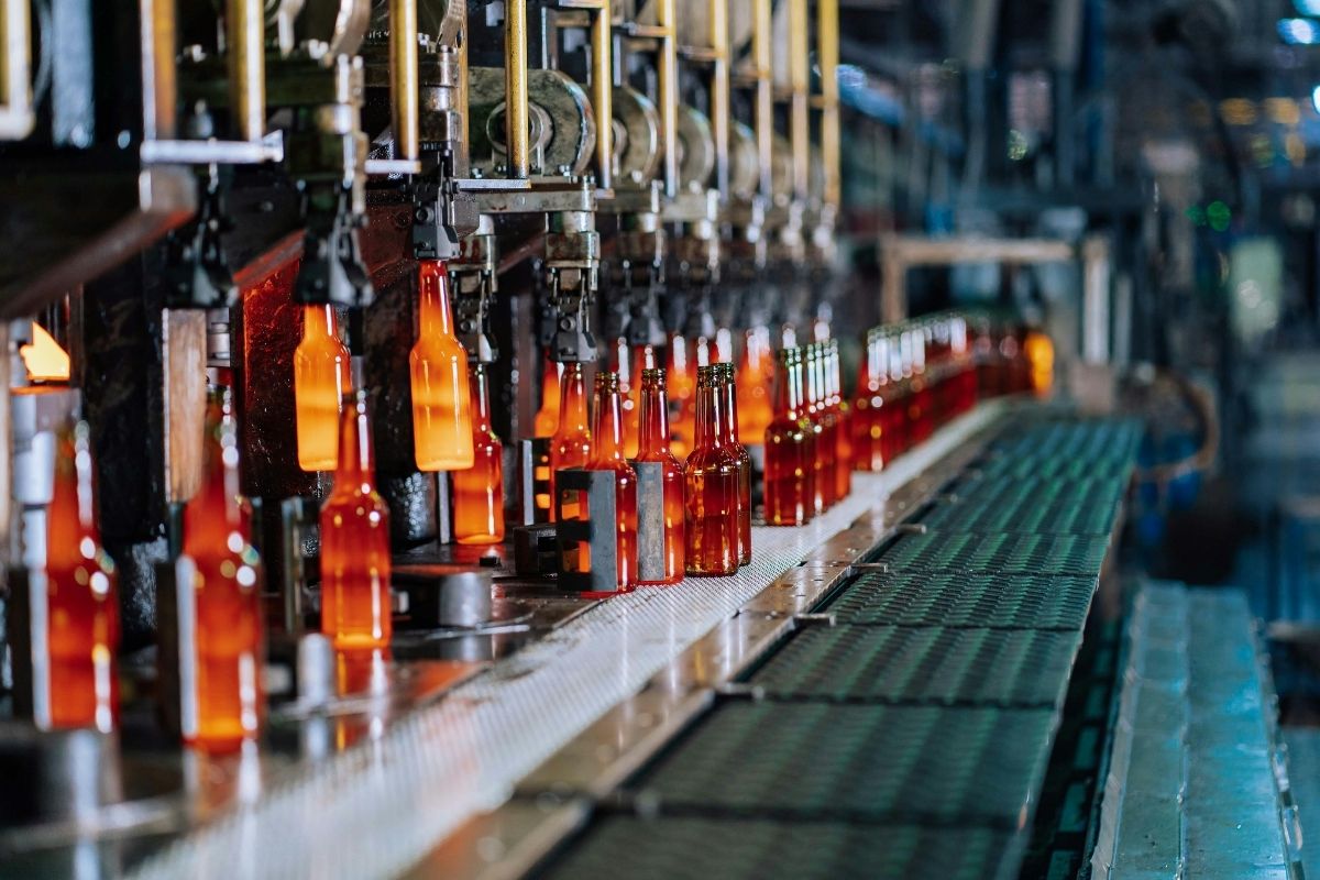 Strategic Benefits Advisors case study regarding health and welfare benefits support for a global packaging company, showing glowing amber glass bottles being formed and transported on an automated manufacturing conveyor line.