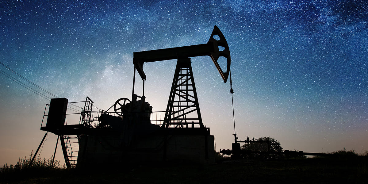 Silhouette of oil pump is pumping crude oil on the oil field in the night under sky with stars and Milky Way. Oil industry equipment